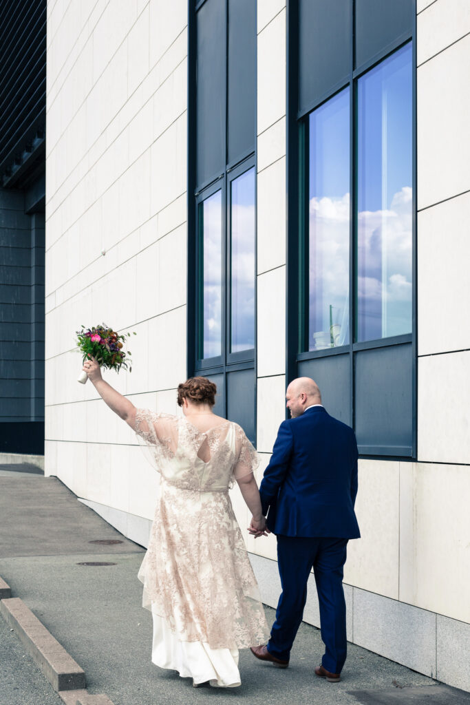 Brudepar på vej væk fra fotografen, med brudebukkent højt over hovedet
